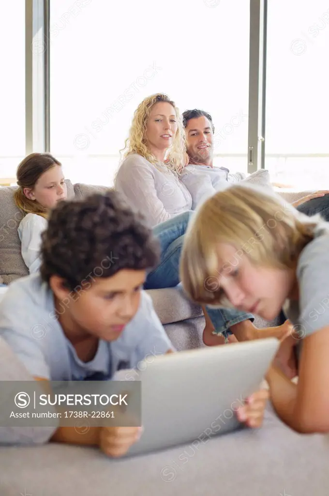 Teenage boy using a digital tablet with his brother and his family in the background