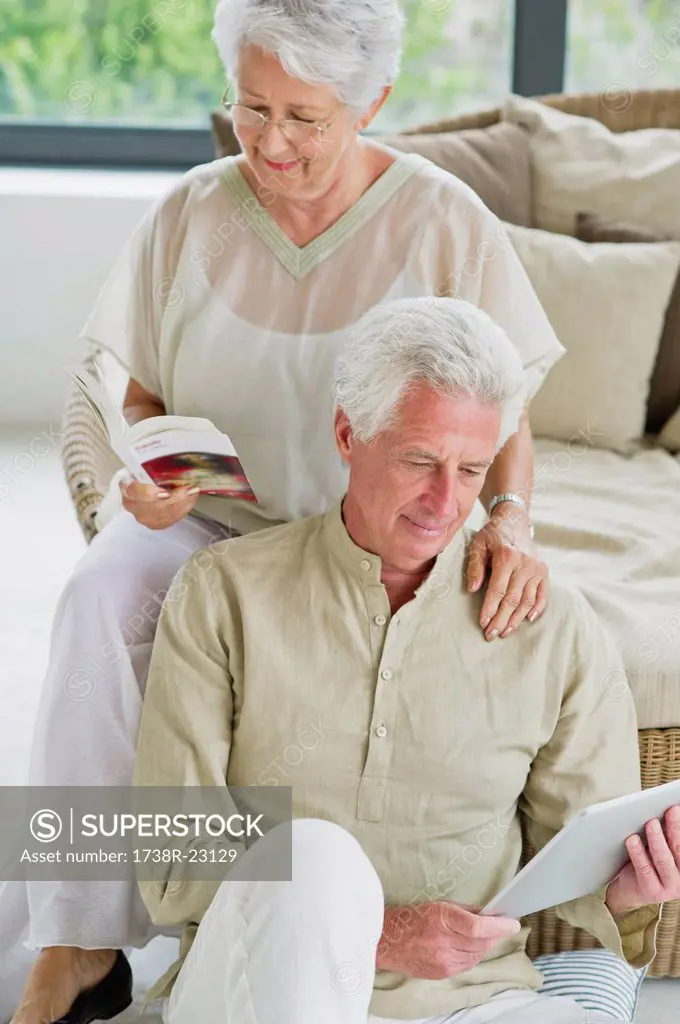 Senior man working on a digital tablet and his wife reading a magazine