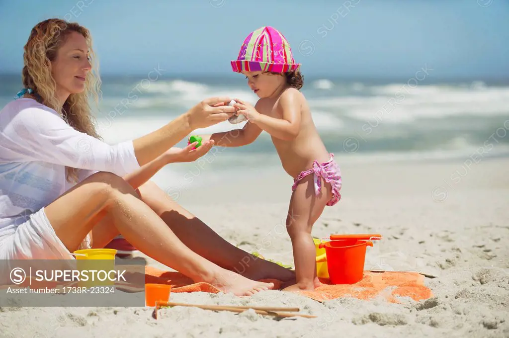 Woman and her daughter playing with pail and shovel on the beach