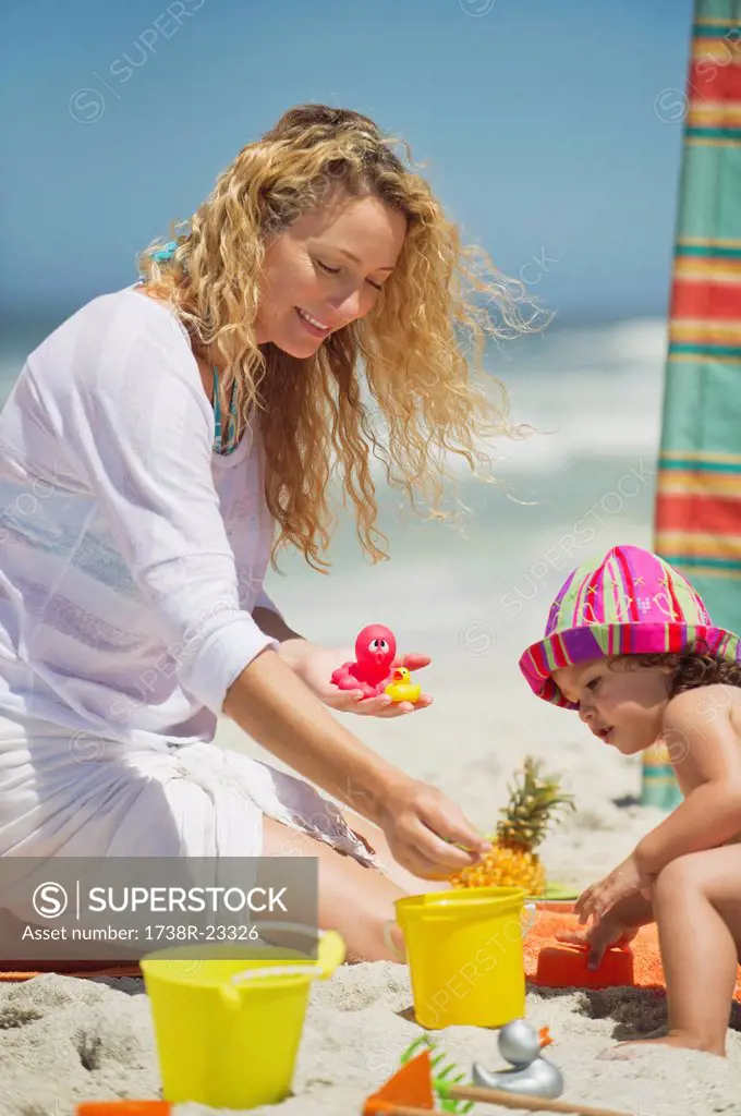 Woman with her daughter playing with pail and shovel on the beach