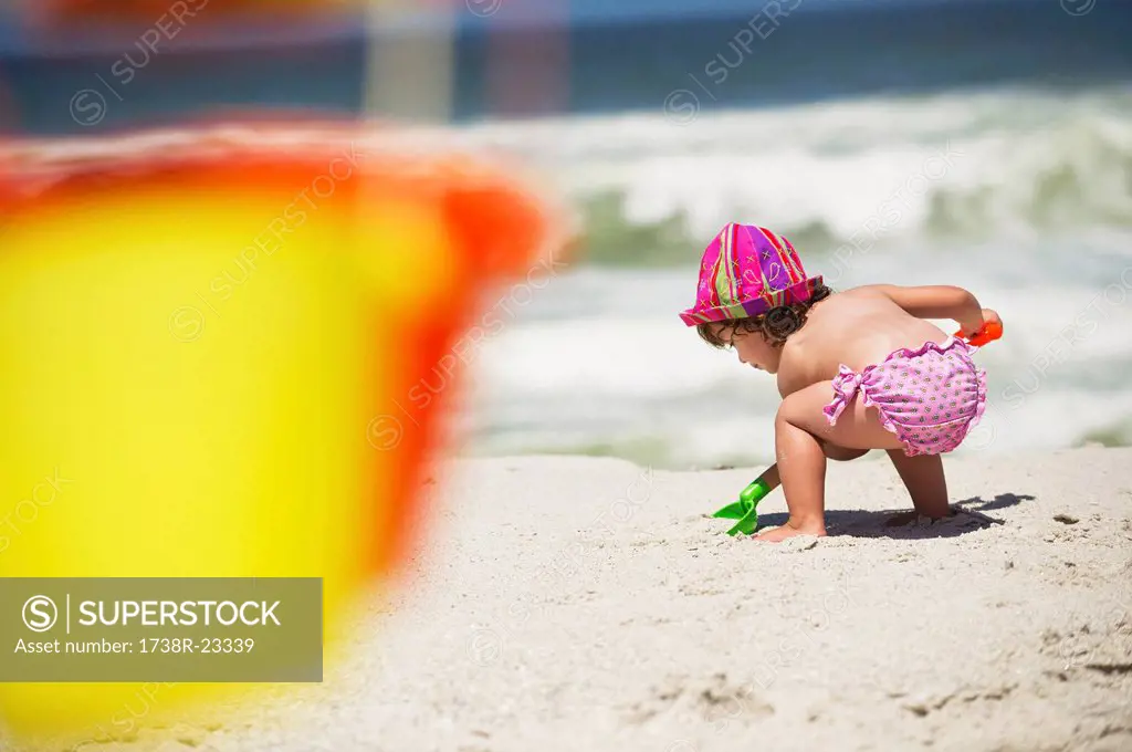 Rear view of a girl digging with a sand shovel on the beach