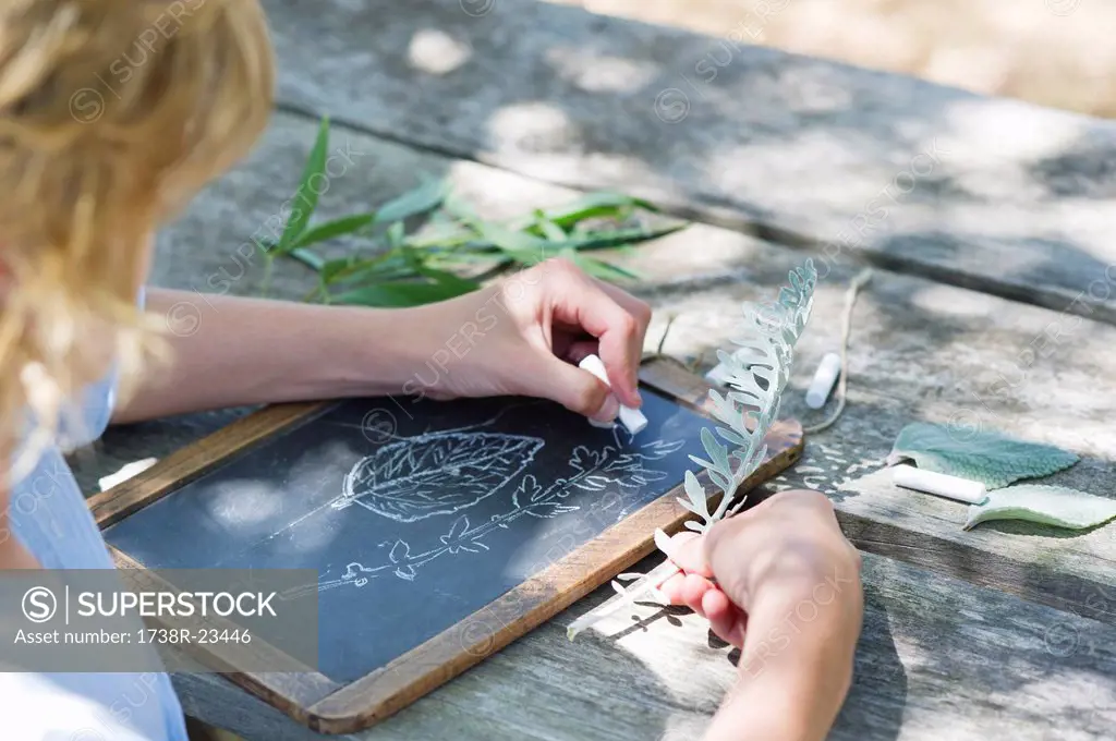 Side profile of a little boy making drawing of leaves on slate outdoors