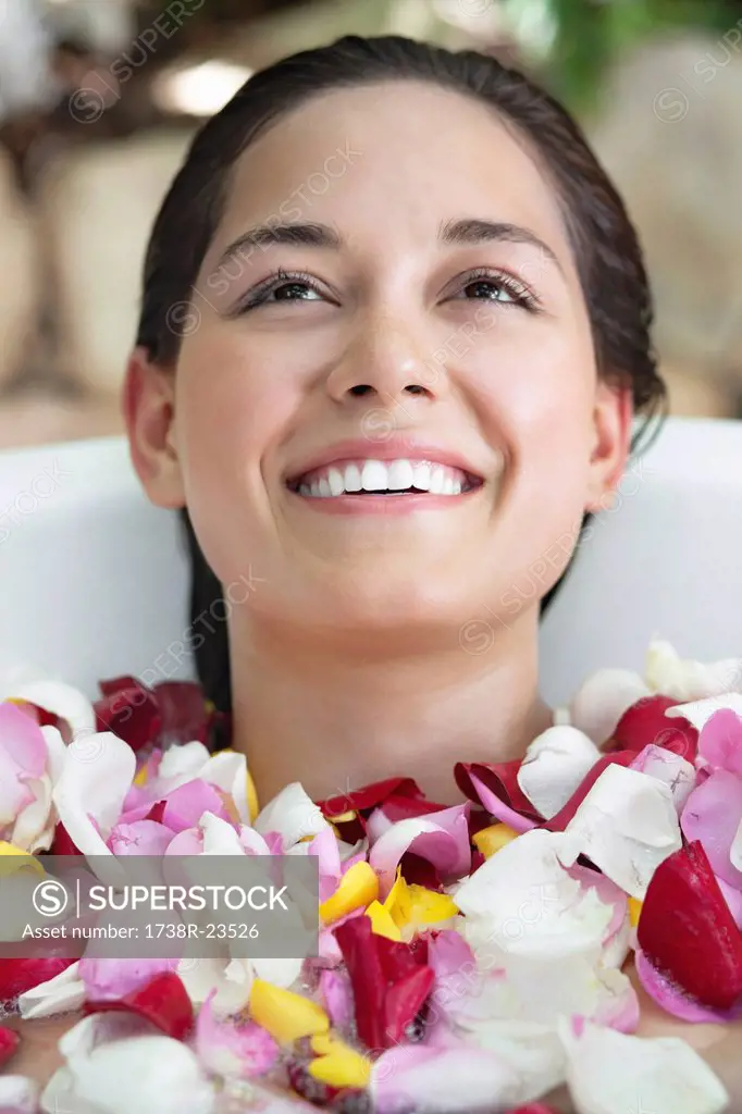 Beautiful young woman relaxing in bathtub with petals