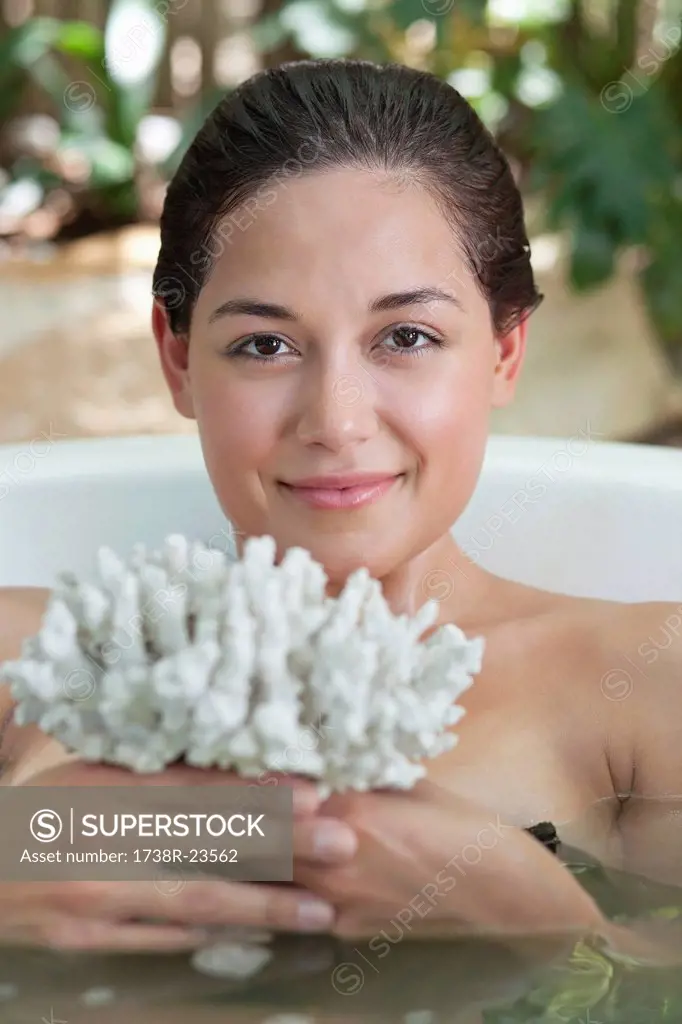 Portrait of a beautiful young woman holding bath sponge in a bathtub