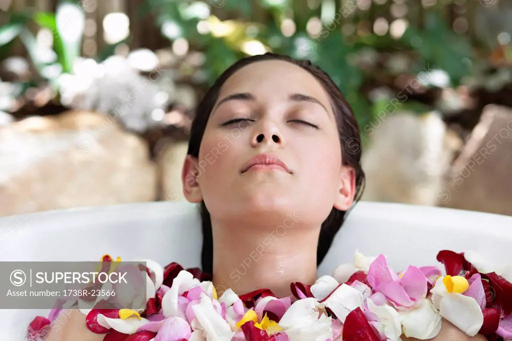 Beautiful young woman relaxing in bathtub with petals