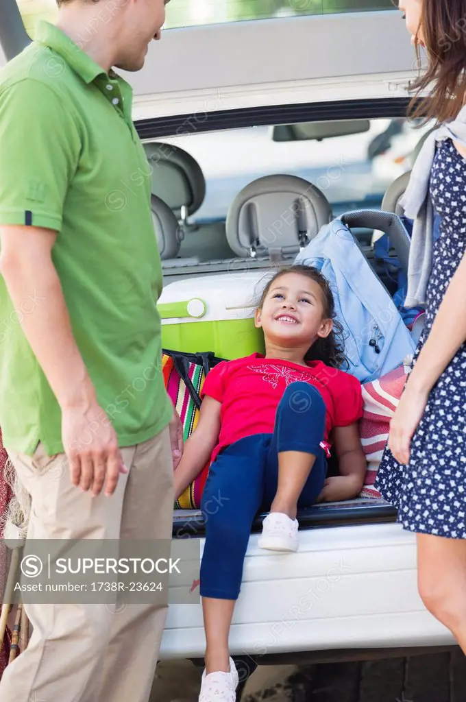 Cute little girl lying in car trunk while parents looking at her