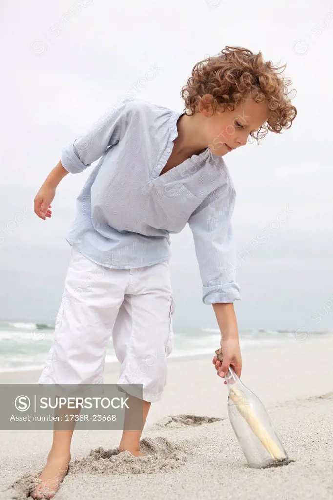Boy reaching for message in a bottle on beach