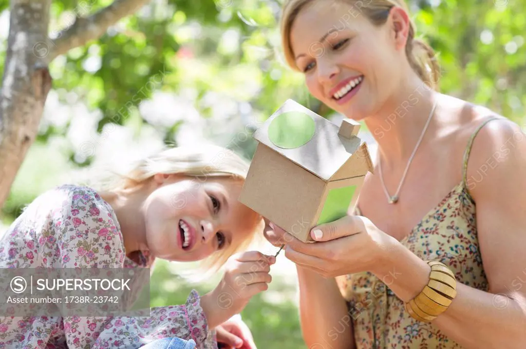 Little girl and her mother looking at dollhouse outdoors