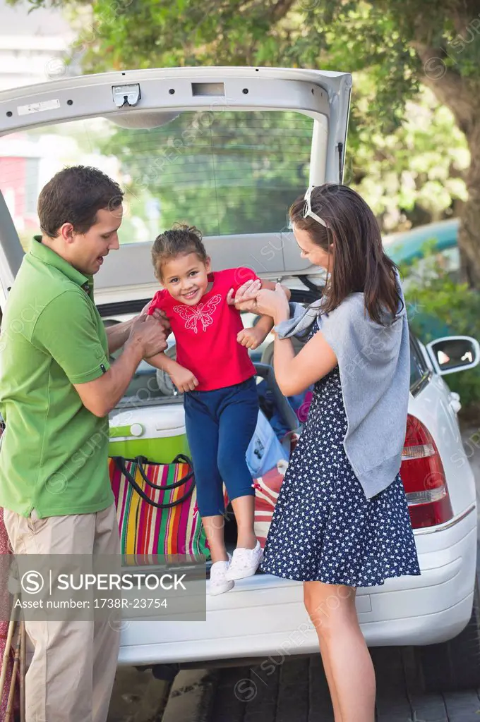 Smiling parents lifting little girl against car