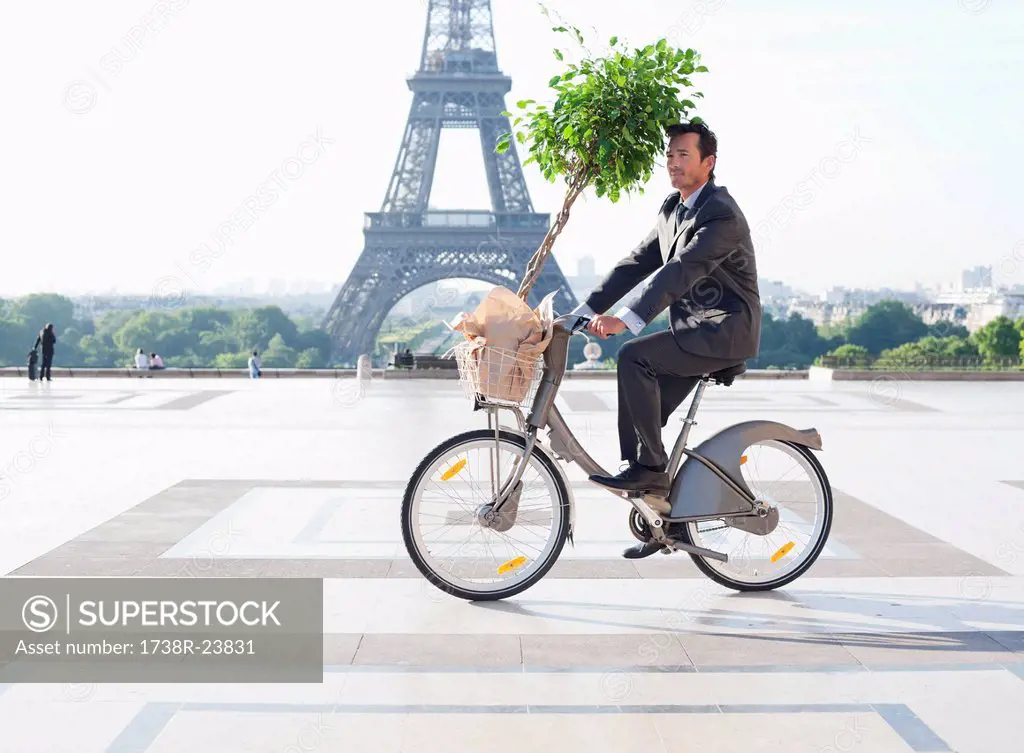 Businessman carrying a plant on a bicycle with the Eiffel Tower in the background, Paris, Ile_de_France, France