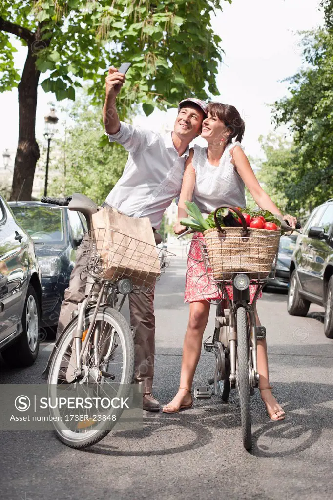 Couple riding bicycles and taking a picture of themselves with a mobile phone, Paris, Ile_de_France, France