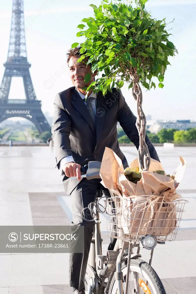 Businessman carrying a plant on a bicycle with the Eiffel Tower in the background, Paris, Ile_de_France, France