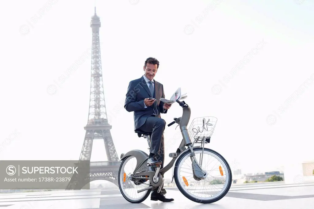 Businessman holding a newspaper and a mobile on a bicycle with the Eiffel Tower in the background, Paris, Ile_de_France, France