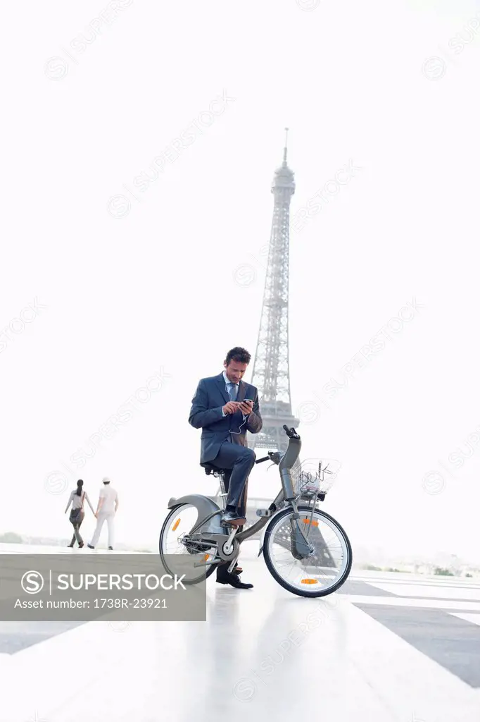 Businessman operating a mobile phone on a bicycle with the Eiffel Tower in the background, Paris, Ile_de_France, France