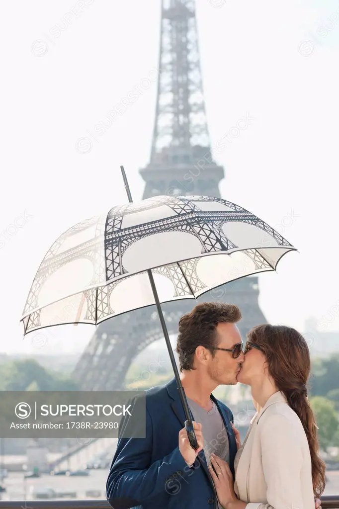 Couple kissing under an umbrella with the Eiffel Tower in the background, Paris, Ile_de_France, France