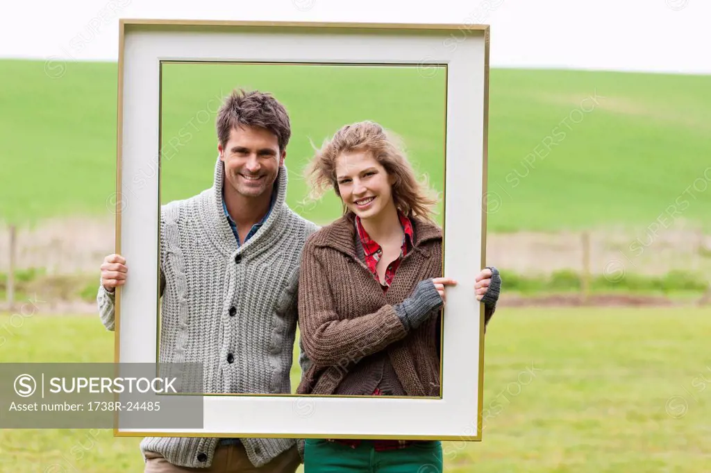 Portrait of a couple holding a frame in a field