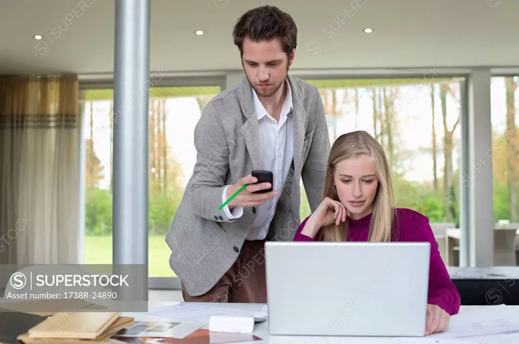 Woman working on a laptop with a man using mobile phone beside her