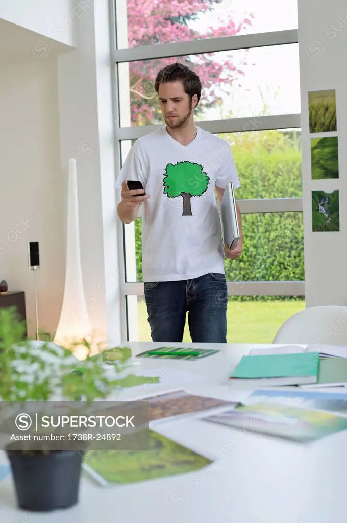 Man using a mobile phone with environment related posters in front of him on a table
