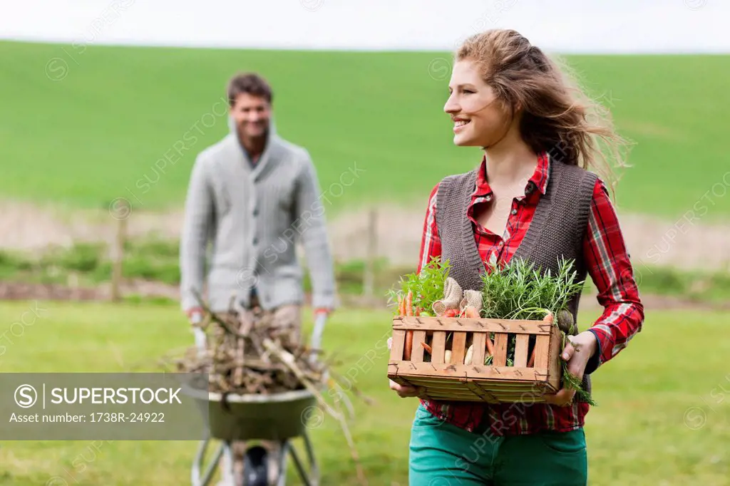 Woman holding a basket of vegetables with her husband collecting firewood