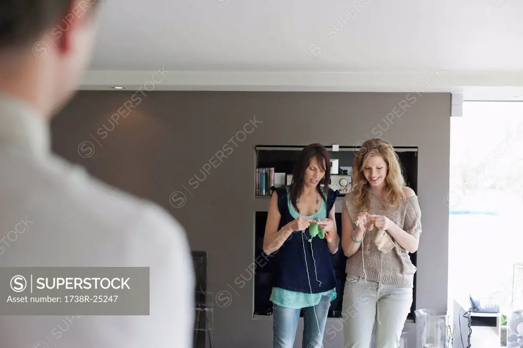 Man looking at two women knitting