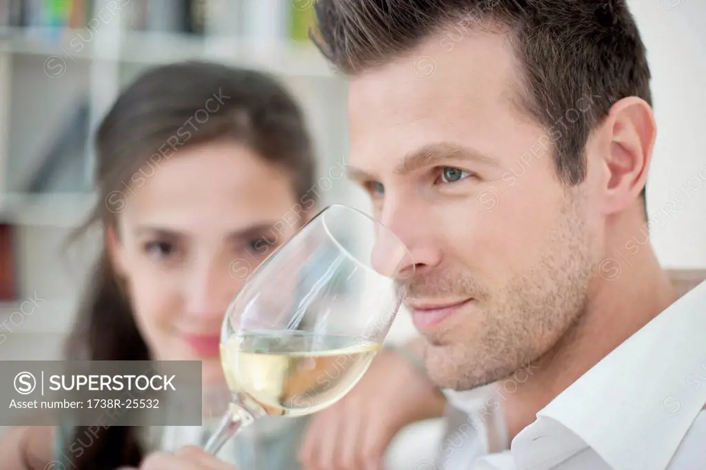 Man drinking white wine with his wife in the background
