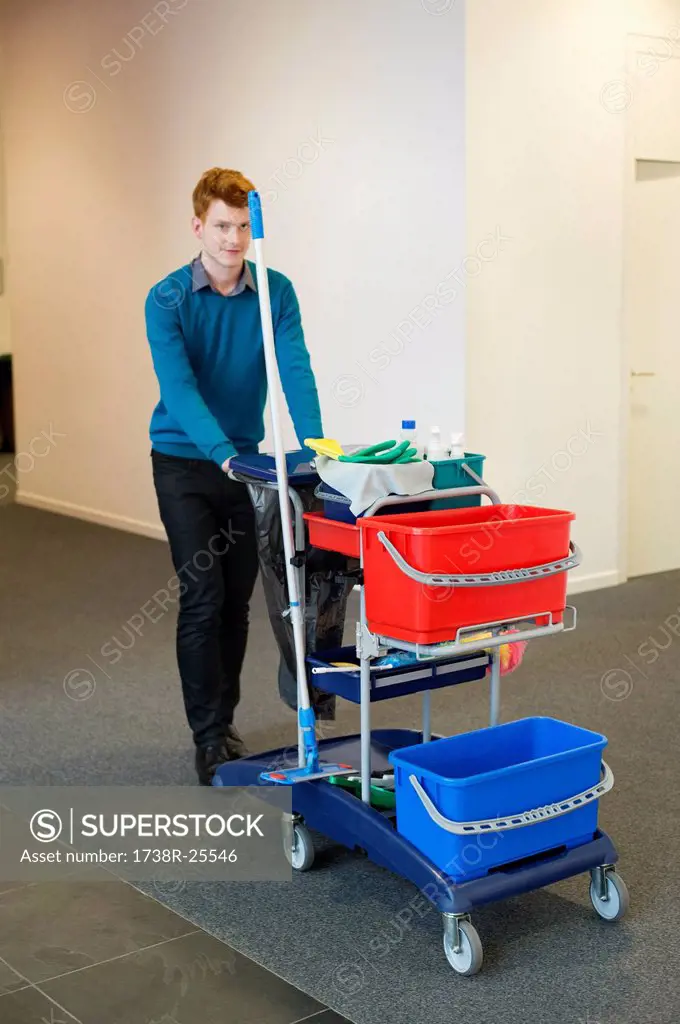 Male cleaner pushing trolley with cleaning equipment