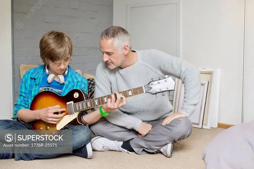 Teenage boy learning guitar with his father at home