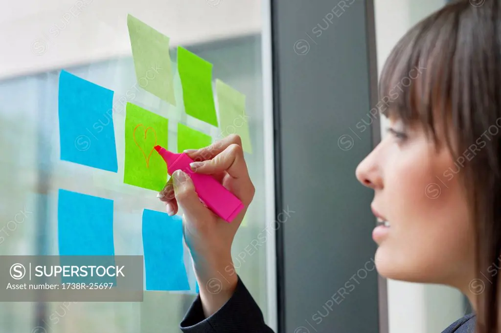 Businesswoman drawing heart shape on an adhesive note in an office