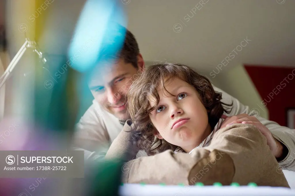Boy thinking while studying with his father at home