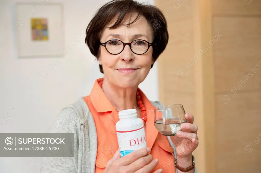 Elderly woman holding bottle of food supplement in the kitchen