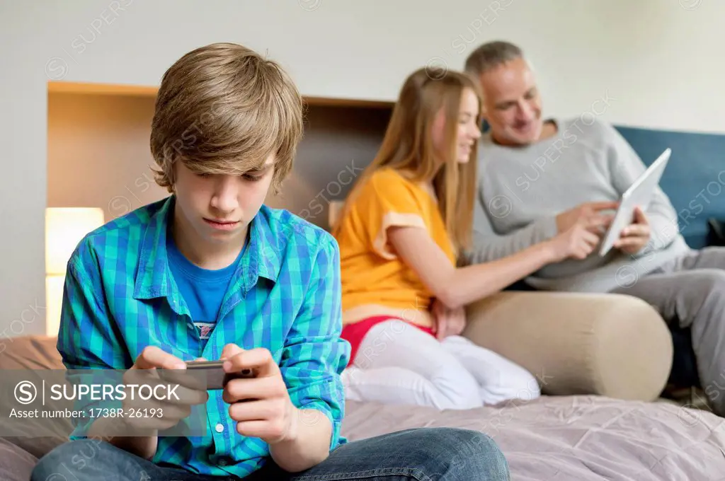 Teenage boy using mobile phone with his father and sister using digital tablet in background