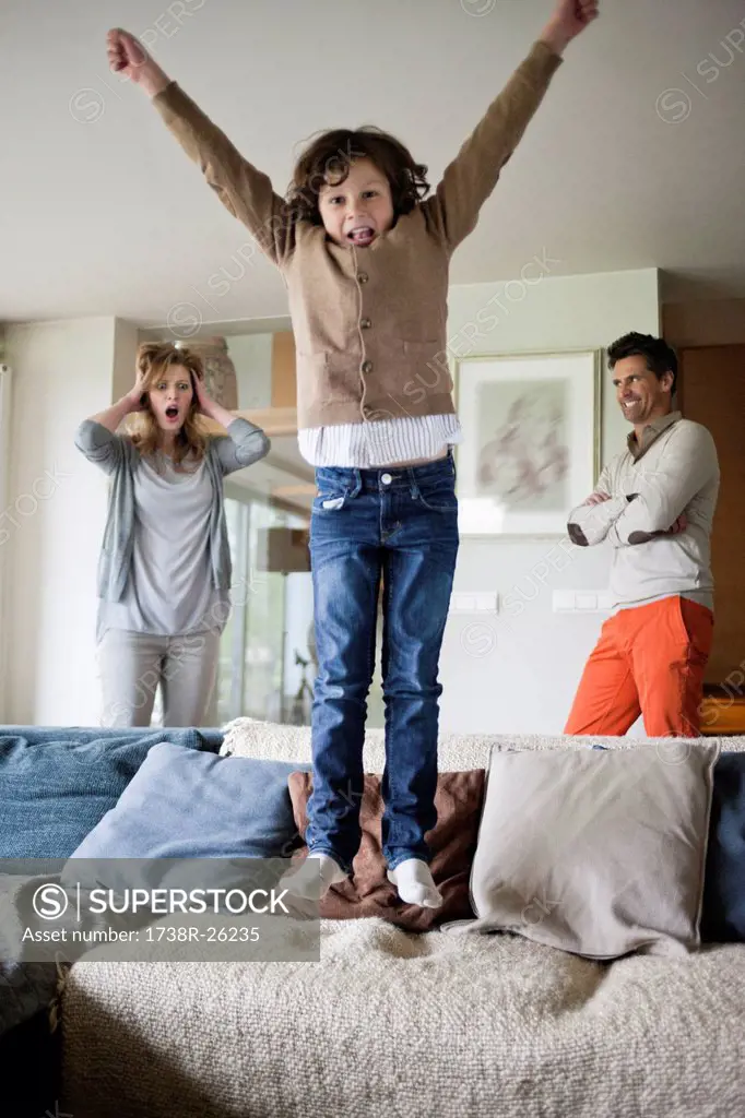 Naughty boy jumping on couch with his parents in the background