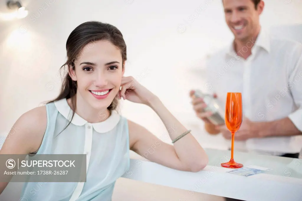 Woman smiling with her husband shaking cocktail in the background