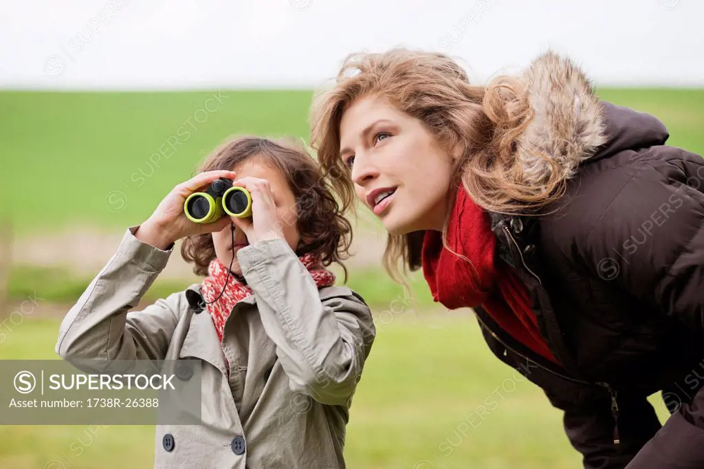 Boy looking through binoculars standing with his mother