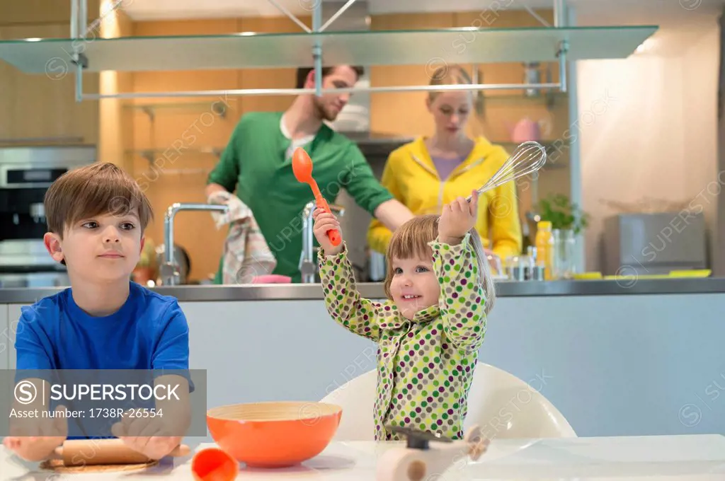 Children cooking in the kitchen with their parents in the background