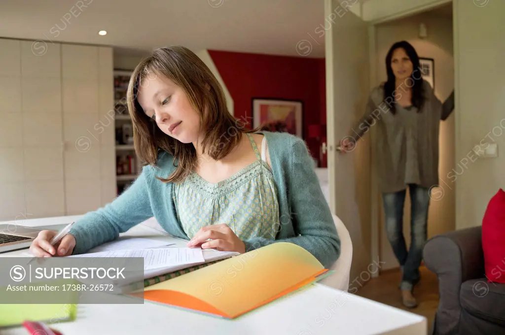Girl studying with her mother standing at door in the background