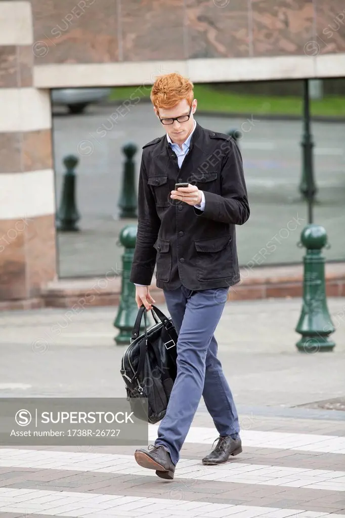 Businessman crossing a road while using a mobile phone