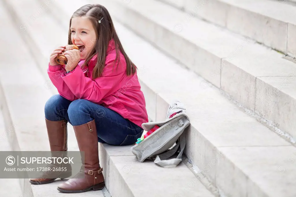 Schoolgirl sitting on the steps and eating pain au chocolat