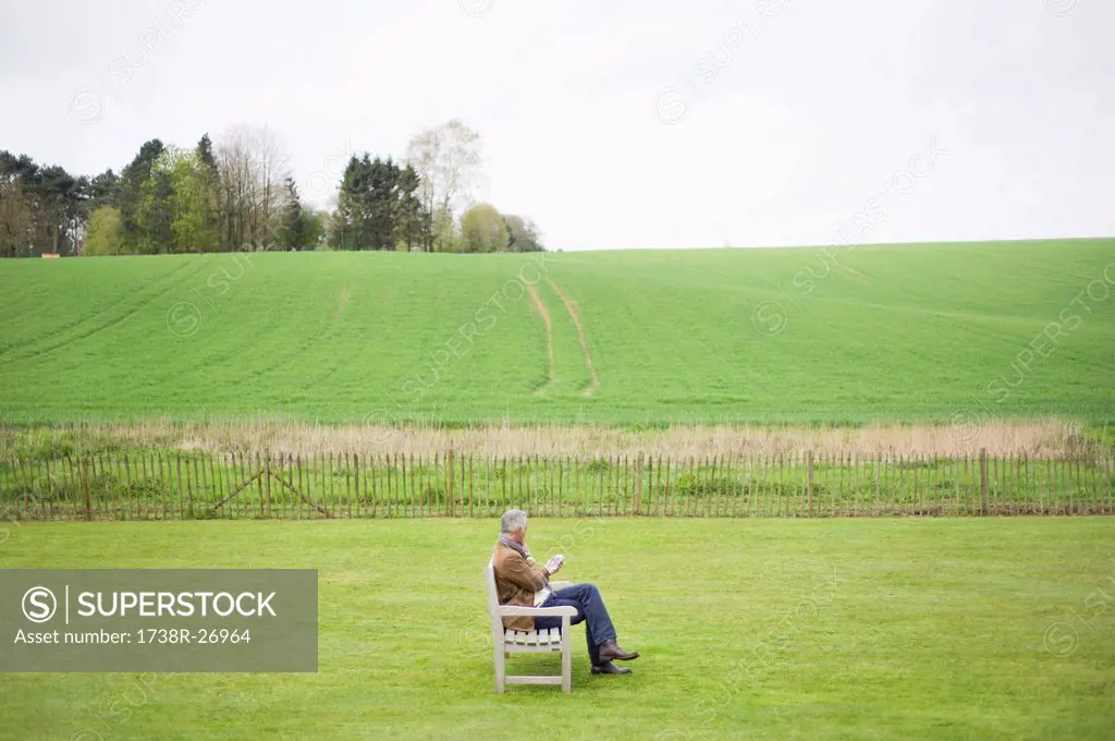 Man sitting on the bench and using a mobile phone in a field