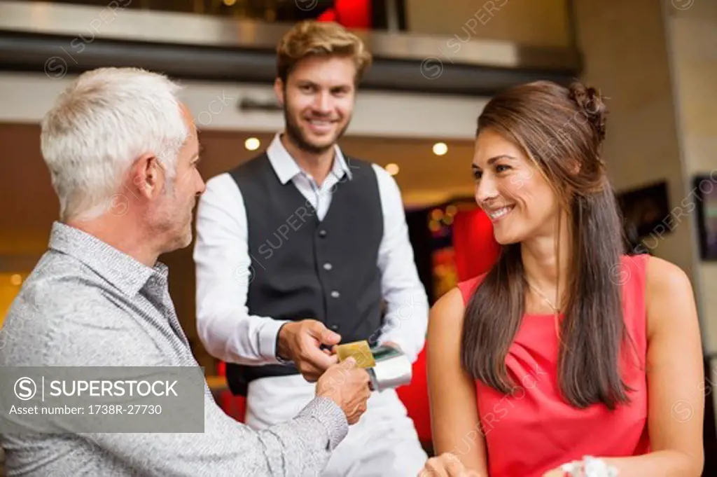 Couple paying with a credit card to a waiter in a restaurant