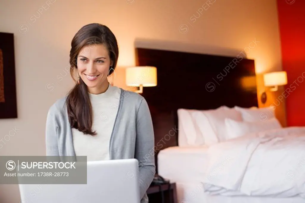 Woman using a laptop in a hotel room and smiling
