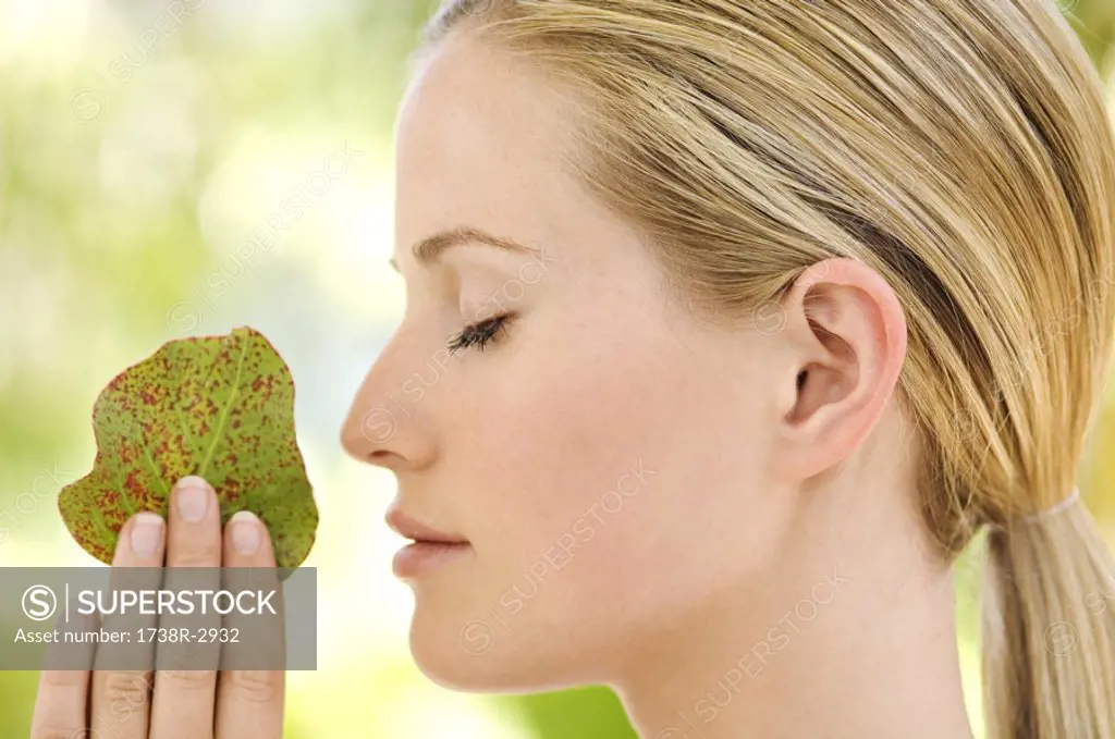 Portrait of a young woman in profile, eyes shut, holding a little leaf, outdoors