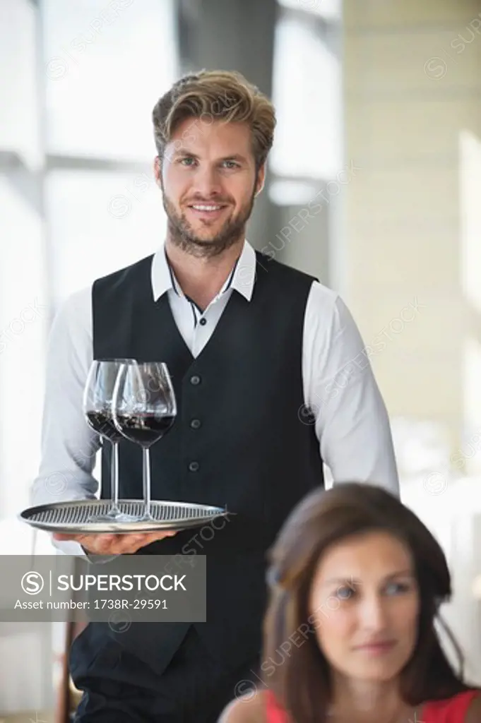 Woman sitting in a restaurant with a waiter holding a tray of wine glasses in the background