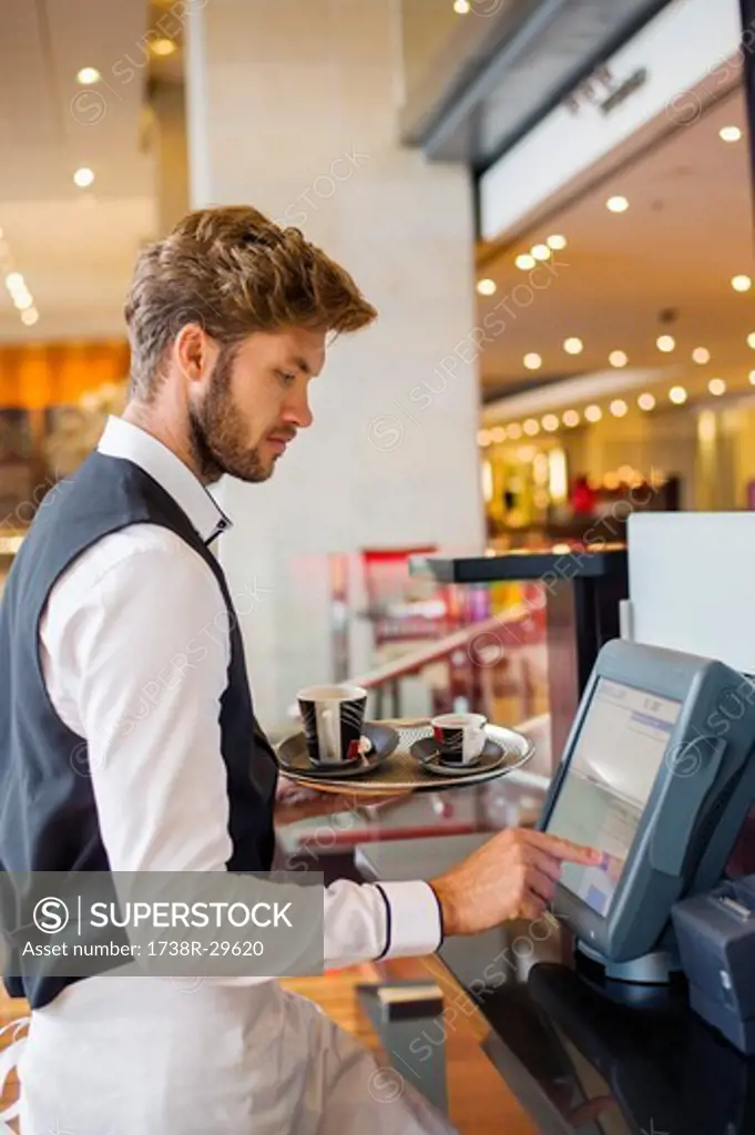 Waiter using a computer at checkout counter in a restaurant