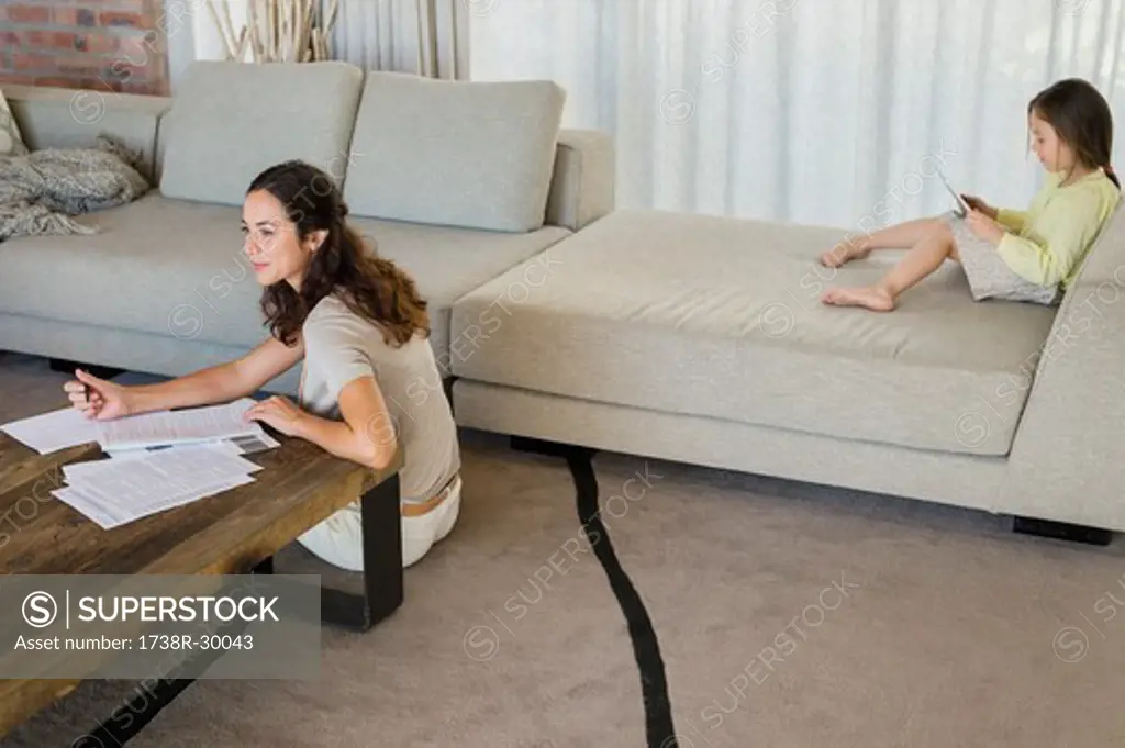 Woman doing paperwork with her daughter using a digital tablet at home