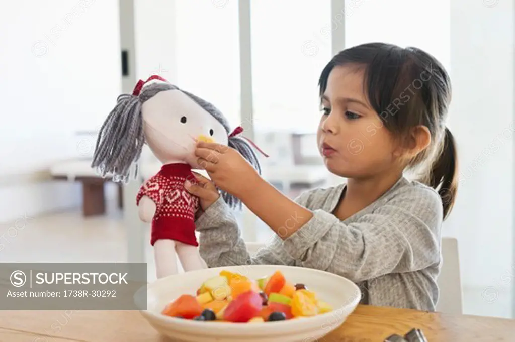 Girl feeding fruit salad to her doll