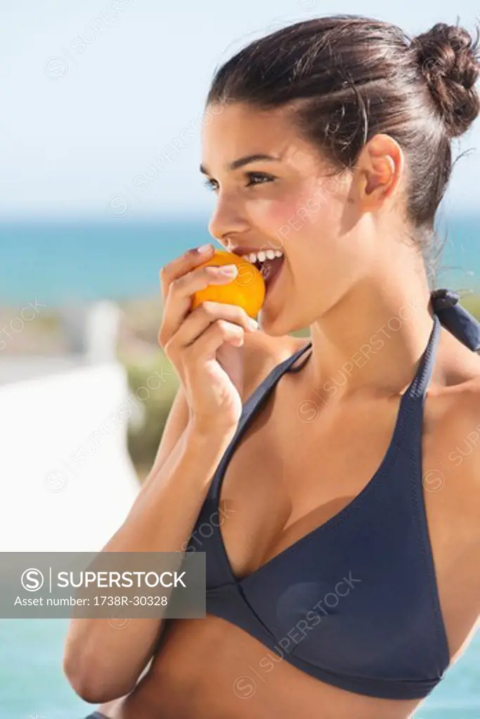 Beautiful woman eating a tomato on the beach