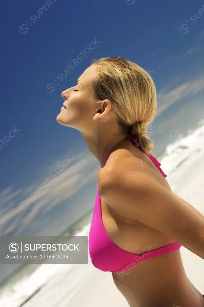 Young woman in pink bikini on beach, head back, eyes closed