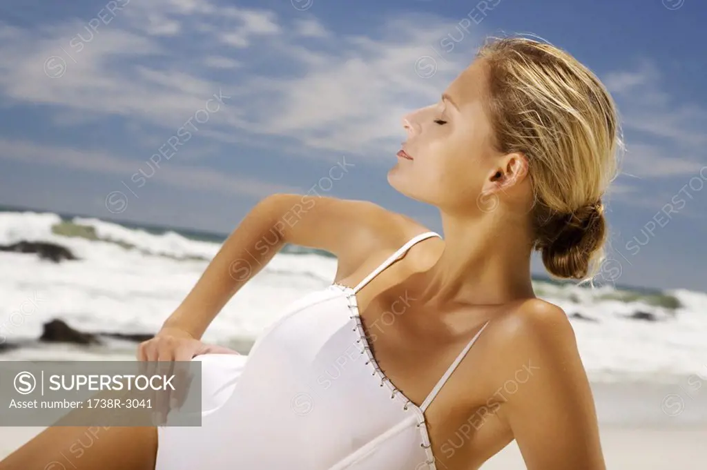 Young woman in swimming costume lying on the beach, eyes closed