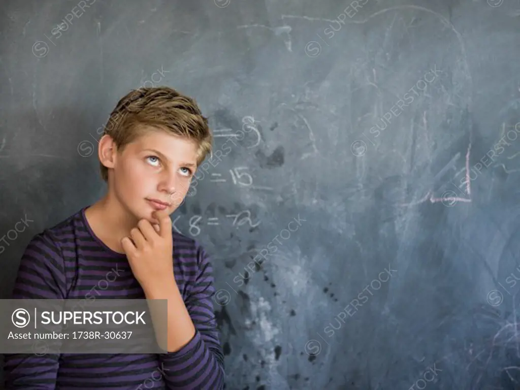 Boy thinking in front of a blackboard in a classroom